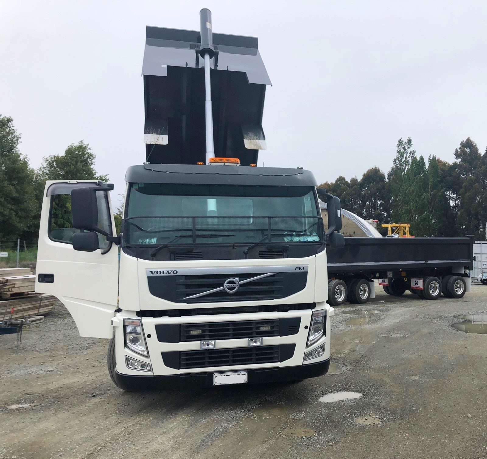 "White Volvo FMX dump truck unloading gravel at a construction site with raised black dump bed